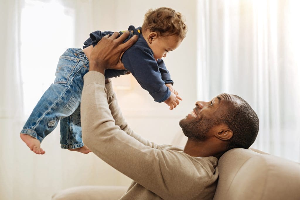 Caring father smiling and amusing his son while sitting on the couch