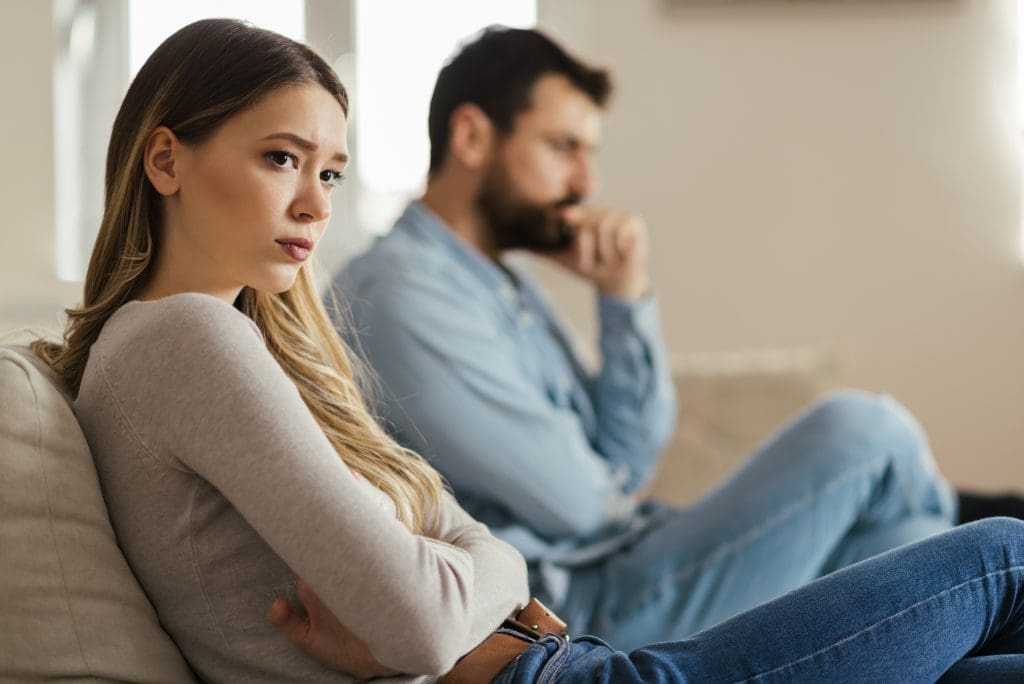 Worried young woman sitting on sofa at home next to husband