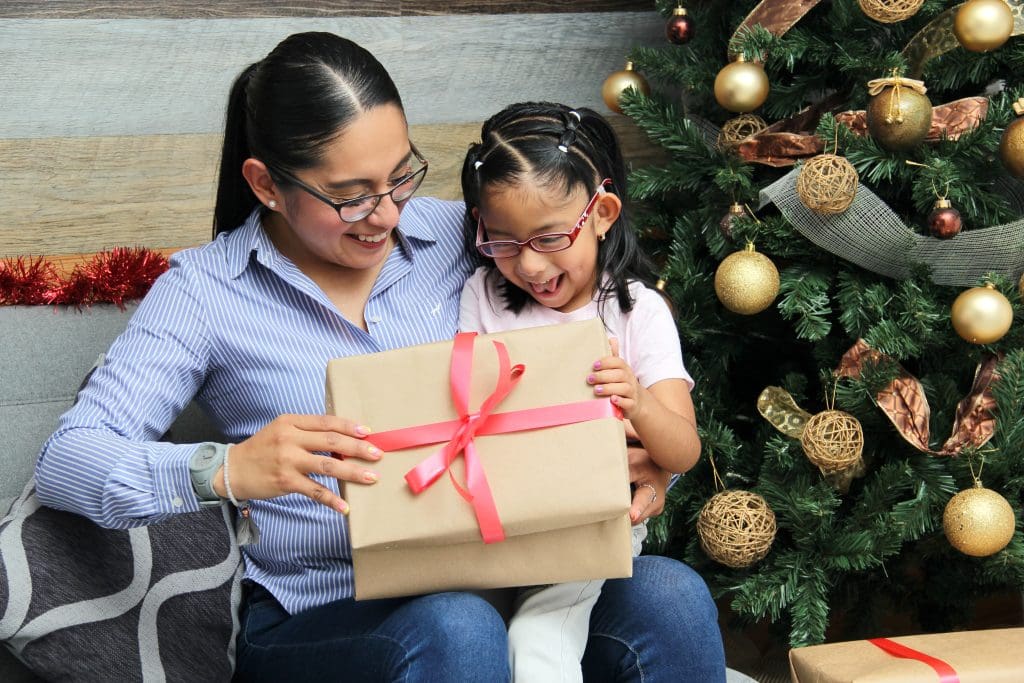 Mother and young daughter opening present next to Christmas tree